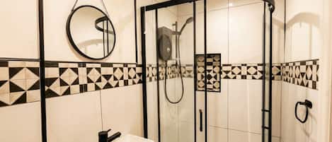 A modern bathroom with a glass-enclosed shower, a white sink with a black faucet, and a mirror with a chain.