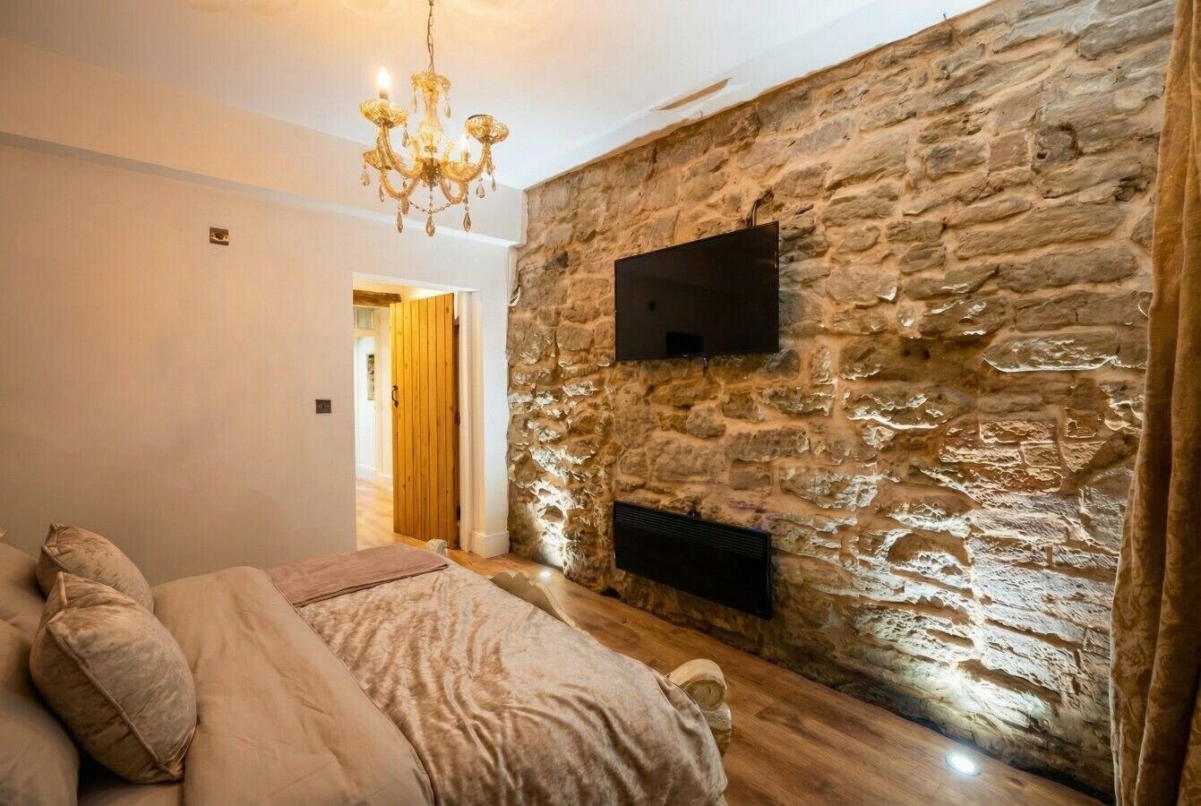 Une chambre avec un mur en pierre, un téléviseur à écran plat, un lustre et un lit avec des oreillers.