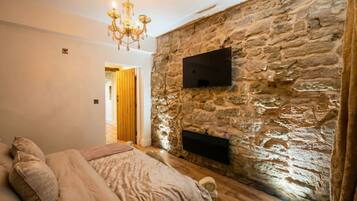 Une chambre avec un mur en pierre, un téléviseur à écran plat, un lustre et un lit avec des oreillers.