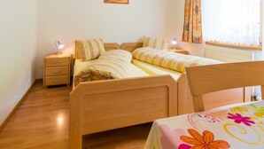 A bedroom with two single beds, a bedside table with a lamp, a wooden headboard, a window with curtains, and a painting on the wall. - Amaryllis Appartement/Fewo 4-Bettwohnung A by Interhome (Saas-Grund)