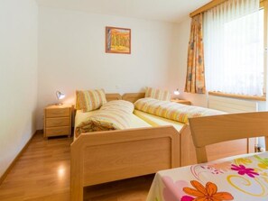 Ein Schlafzimmer mit zwei Einzelbetten, einem Nachttisch mit Lampe, einem Holzkopfstück, einem Fenster mit Vorhängen und einem Gemälde an der Wand.