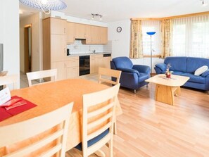Ein modernes Wohnzimmer mit Essbereich, einem blauen Sofa und einer Küche im Hintergrund.