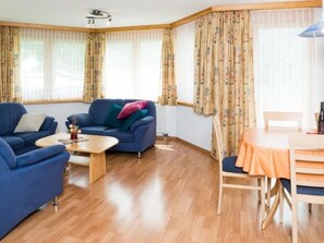 Ein Wohnzimmer mit blauem Sofa, einem Holztisch und einem Essbereich mit Tisch und Stühlen.
