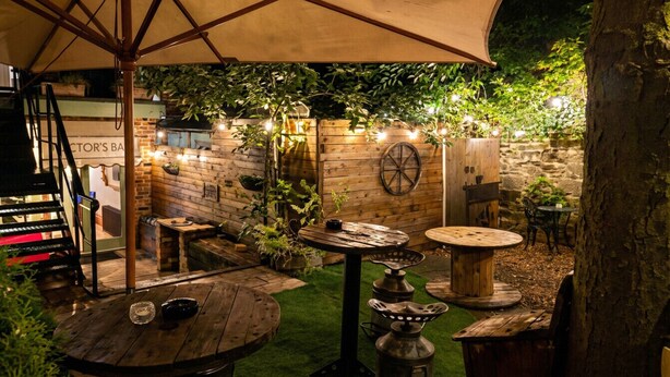 Ein Terrassenbereich im Freien mit Holztischen und -stühlen, einer Backsteinmauer und Lichterketten.