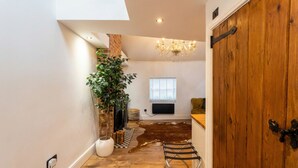 Ein Zimmer mit Holzboden, einer großen Pflanze, einem Chandelier, einer Holztür und einem Fenster mit Jalousien.