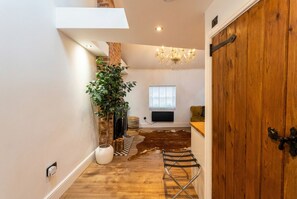 A room with a wooden floor, a large plant, a chandelier, a wooden door, and a window with blinds. - Vaulted ceilings, open fireplace and weekend cocktails included (Castle Donington)
