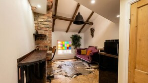 Une pièce avec un parquet en chevrons, un mur en briques, un plafond en bois, un canapé violet, une télévision et une porte.