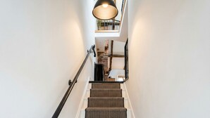 Un escalier recouvert d’une moquette à rayures et doté d’une rampe noire, menant à un palier où est suspendu un luminaire.