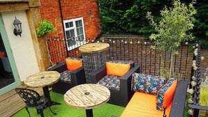 Une terrasse dotée de meubles en osier, de deux tables rondes en bois et d’un mur en briques.