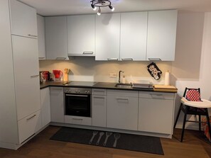 Eine moderne Küche mit weißen Schränken, einem Einbauofen, einem Spülbecken und einer kleinen Essecke mit Hochstuhl.