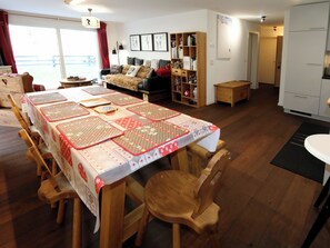 Ein Essbereich mit einem langen Tisch, der mit einer gemusterten Tischdecke bedeckt ist, umgeben von Holzstühlen.