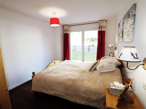 Ein Schlafzimmer mit einem großen Bett, einem Nachttisch mit Lampe und einem Fenster mit Vorhängen.