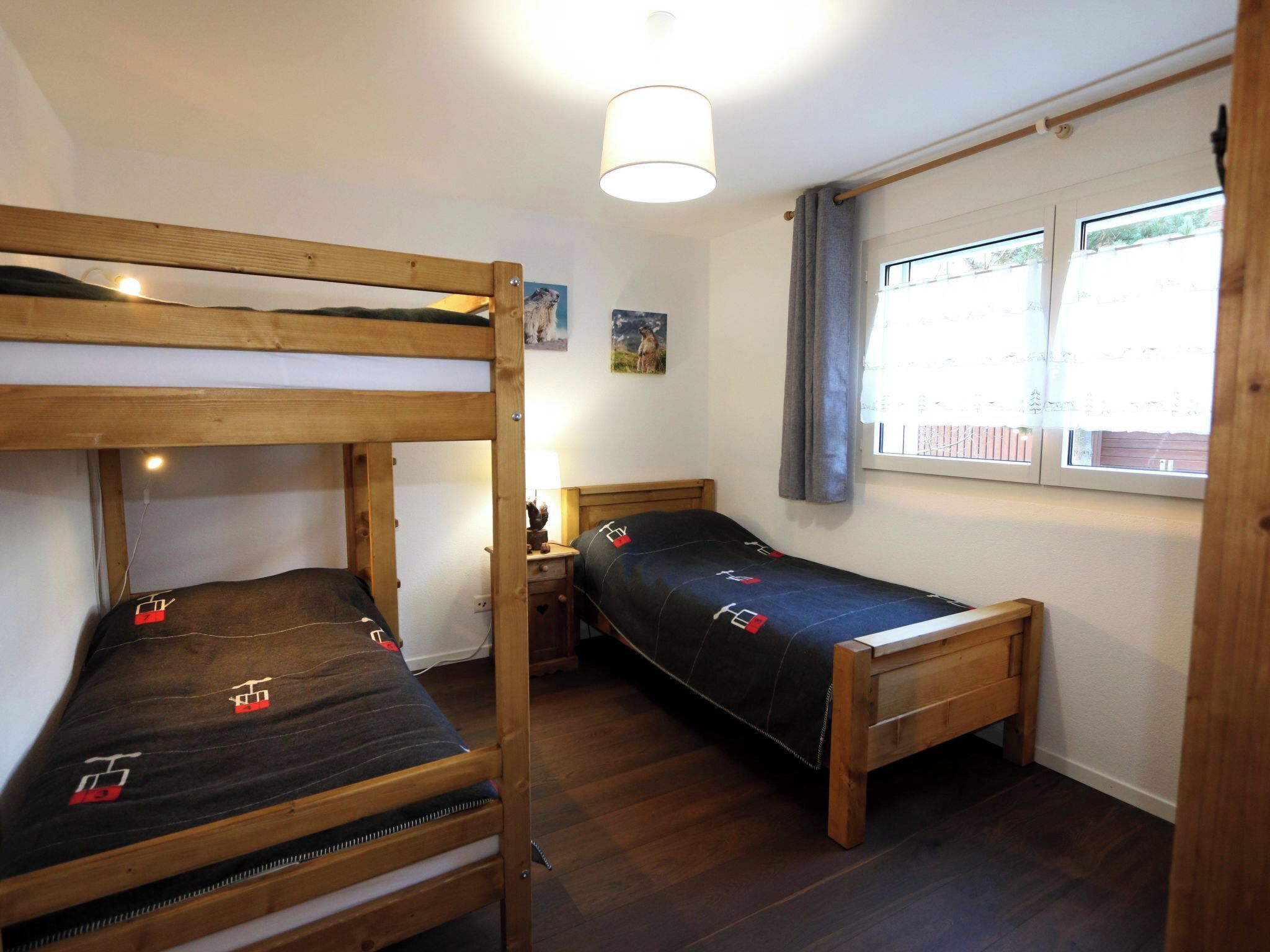 Una habitación con dos literas, una mesita de noche con lámpara y una ventana con cortinas.