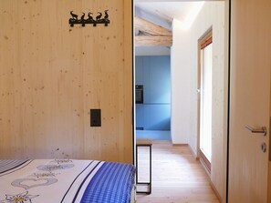 Une chambre à coucher avec un lit, un mur en bois orné de la silhouette d’une chèvre, et une vue sur une cuisine moderne.