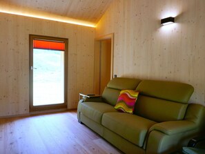 Ein Zimmer mit einem grünen Sofa, einem kleinen Tisch, einer Tür mit Fenster und einer Wandleuchte.