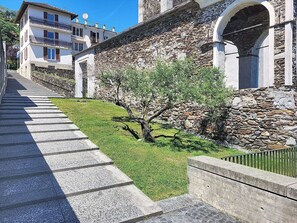 Ein Steinhaus mit einer Treppe, die zu einer Tür führt, ein kleiner Baum im Vordergrund und ein klarer, blauer Himmel.