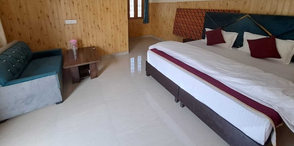 A hotel room with a bed, a sofa, a small table, and wooden walls.