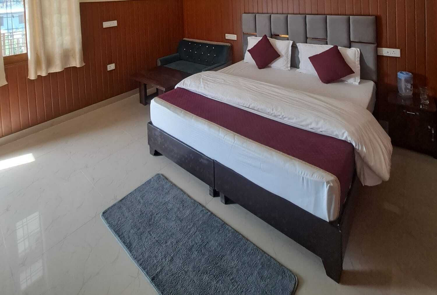 A hotel room with a large bed, a bedside table, a bench, and a view of the outdoors.