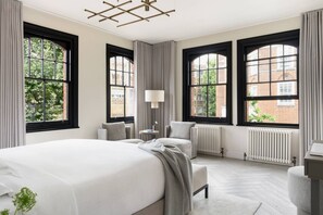 Une chambre d’hôtel avec un grand lit, deux fauteuils, une petite table et un radiateur.