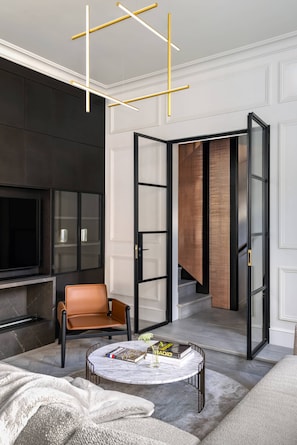 A modern living room with a sofa, coffee table, and a television. There is a staircase with a patterned rug leading to an upper level. - Emery Hill Street by onefinestay (London)