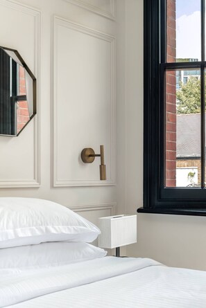 A hotel room with a bed, a nightstand, a lamp, a door, and a window with a view of the outside. - Emery Hill Street by onefinestay (London)