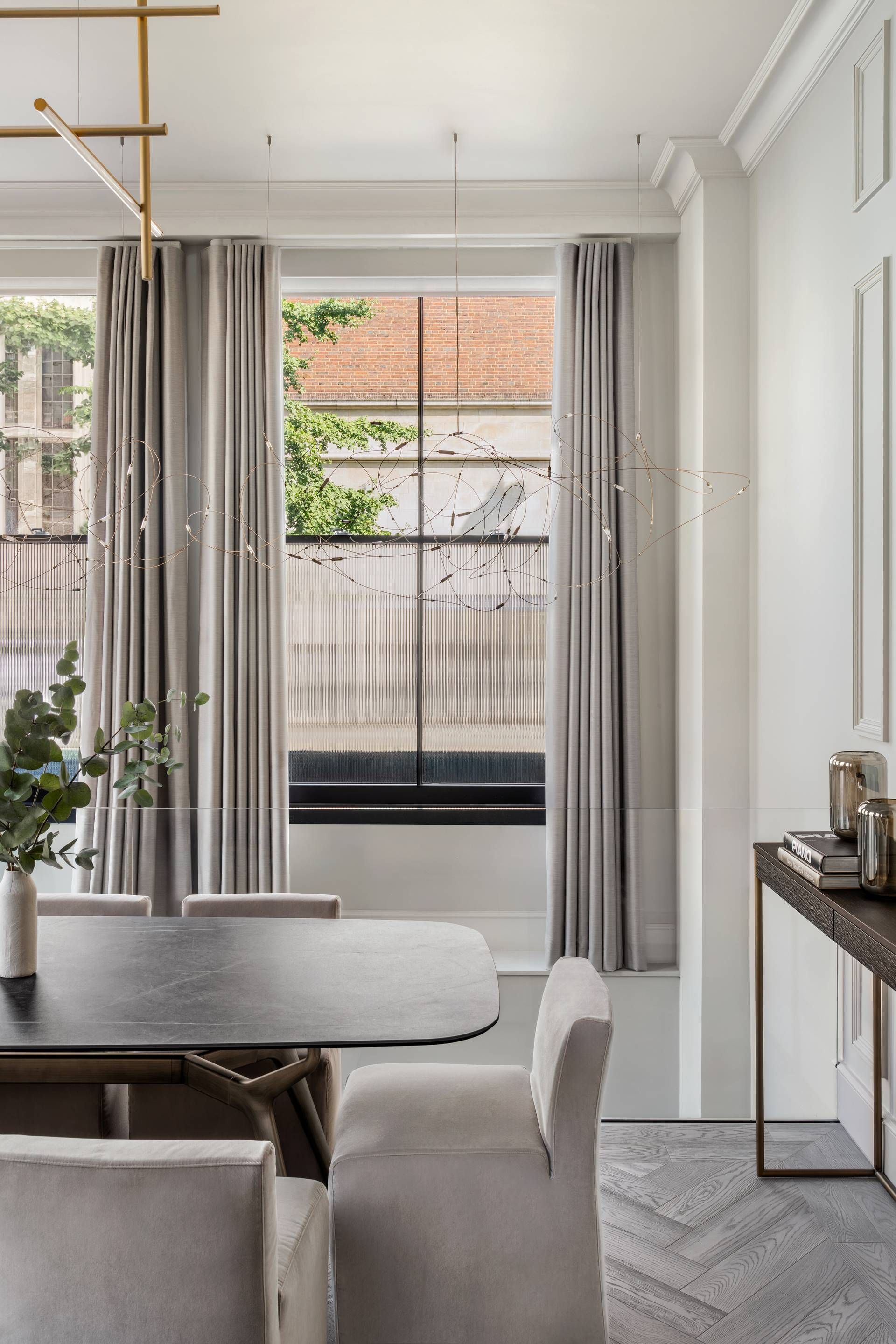 A modern dining area with a table, chairs, and a view of a brick building through a window with curtains.