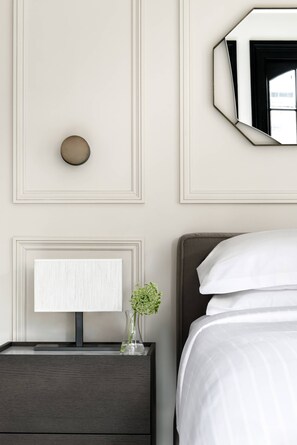 Une chambre d’hôtel bien rangée, avec un lit, une table de chevet dotée d’une lampe et un miroir fixé au mur.