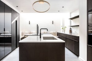 A modern kitchen with a central island, dark cabinetry, and a minimalist design. - Emery Hill Street by onefinestay (London)