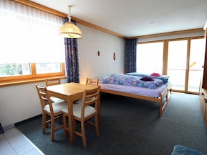 Ein Zimmer mit einem Bett, einem Tisch, Stühlen, einer Pendelleuchte und Blick durch ein Fenster.