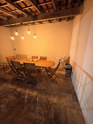 Ein runder Holztisch mit Stühlen, ein Mülleimer und eine Decke mit freiliegenden Balken und hängenden Lampen.