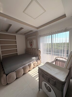 Ein Schlafzimmer mit einem Bett, einem Sessel, einem Fenster mit Vorhängen und Blick ins Grüne.