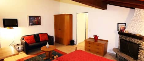 Una habitación acogedora con una cama, un sofá, un armario de madera, chimenea y televisor.