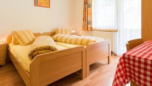 A room with two wooden beds, a small table with a checkered tablecloth, and a window with curtains. - Amaryllis Appartement/Fewo 4-Bettwohnung B by Interhome (Saas-Grund)