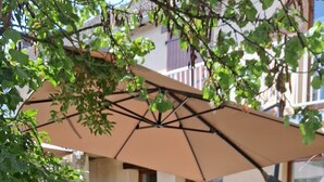 Un espace extérieur aménagé avec une table et des chaises, une terrasse couverte et des plantes en pot.
