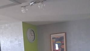 Une pièce comprenant un lit, un banc, une petite table, une horloge murale et un tableau encadré.