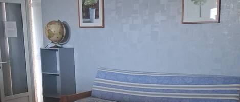 Une pièce avec un plancher en bois, un canapé orné d’un coussin à rayures, une petite table et deux tableaux encadrés accrochés au mur.