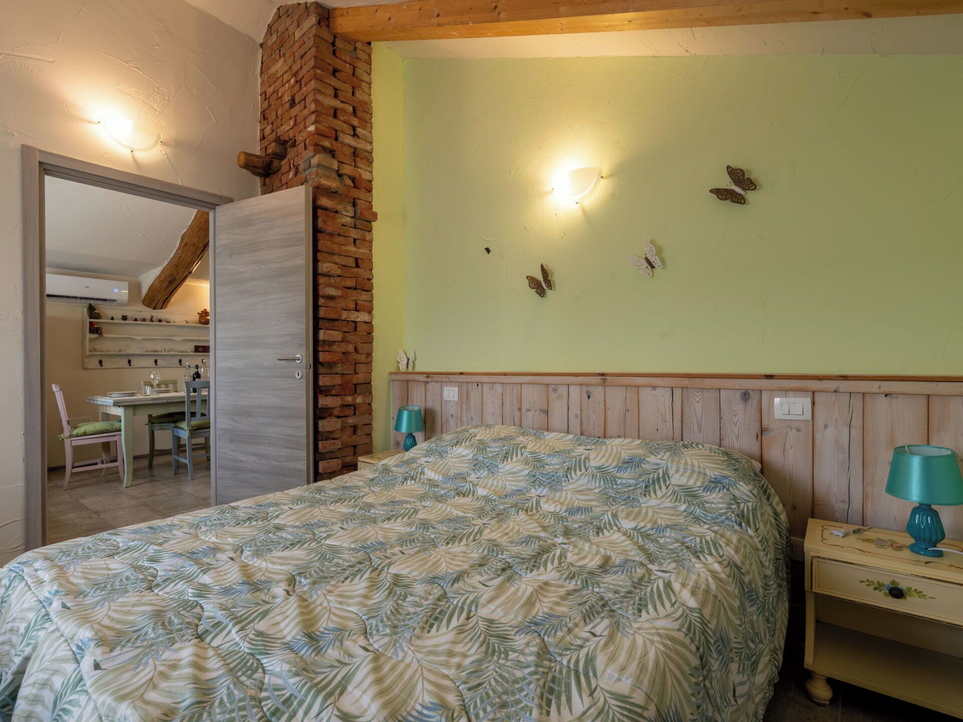 Una camera da letto con un letto, un comodino, una lampada, una parete in mattoni e una decorazione a forma di farfalla.