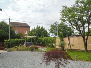 Un patio trasero residencial con un patio, una casa de ladrillo y un jardín cercado.