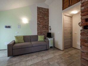 Una sala de estar con sofá, televisor, un muro de ladrillo decorativo y una puerta.
