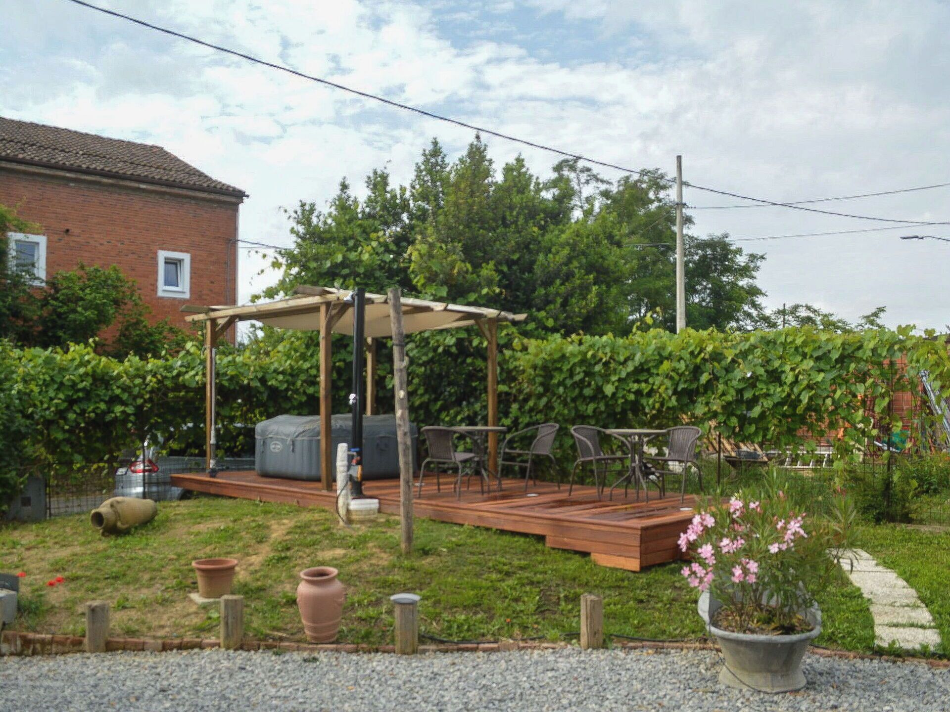 Un cortile con un terrazzo in legno, mobili da esterno, un barbecue e un pergolato.