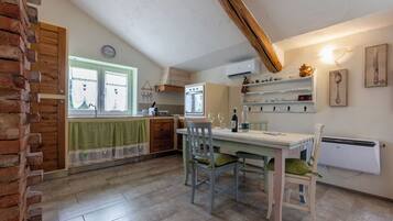 Une cuisine avec un coin repas, comprenant un mur en briques, des armoires en bois, une fenêtre avec des rideaux et une table avec des chaises.