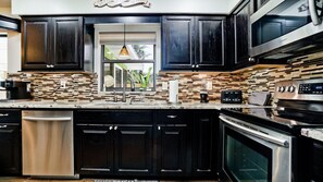 Cozinha moderna com armários escuros, lava-louças de aço inoxidável e micro-ondas Samsung.