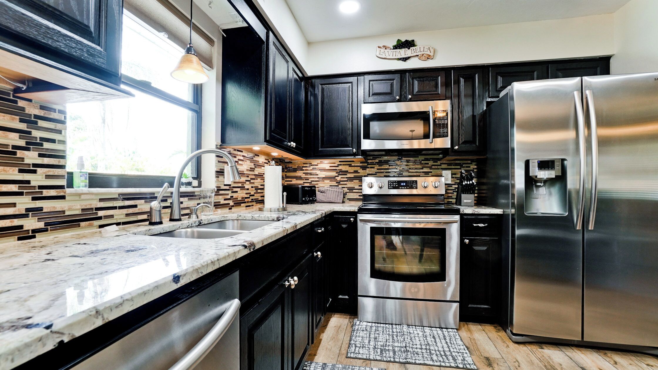 A modern kitchen with dark cabinets, stainless steel appliances, a marble countertop, and a built-in oven.