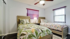 A bedroom with two beds, a ceiling fan, a window with blinds, and a nightstand with a lamp. - 3-bedroom house in tranquil Bradenton with tropical vibes (Bradenton)