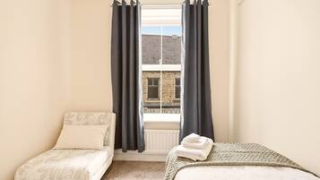 Ein Schlafzimmer mit zwei Betten, einem fensterbelaubten Fenster, einem Heizkörper und Blick auf ein Gebäude.