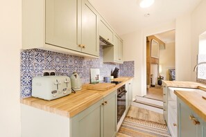 A compact kitchen with a wooden countertop, two electric toasters, and a patterned backsplash.