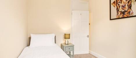 A hotel room with a bed, a nightstand with a lamp, a door, and a framed picture on the wall.