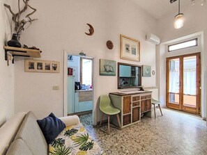 Ein Wohnzimmer mit einer Couch, einem Schreibtisch mit Computer, einem Sessel und einem Fenster mit Vorhängen.
