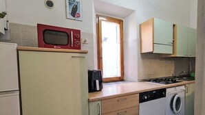 Cocina compacta con microondas, cafetera, lavadora y ventana con vistas.