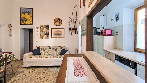 Una sala de estar con sofá, mesa de centro y una zona de cocina con electrodomésticos.